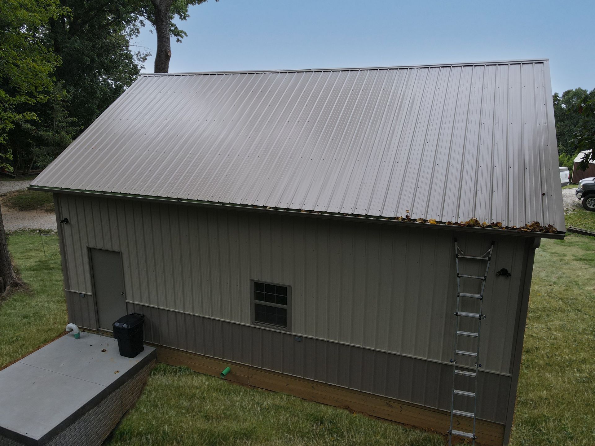 Gray metal shed with a sloped roof and ladder, viewed from outside in a grassy yard.