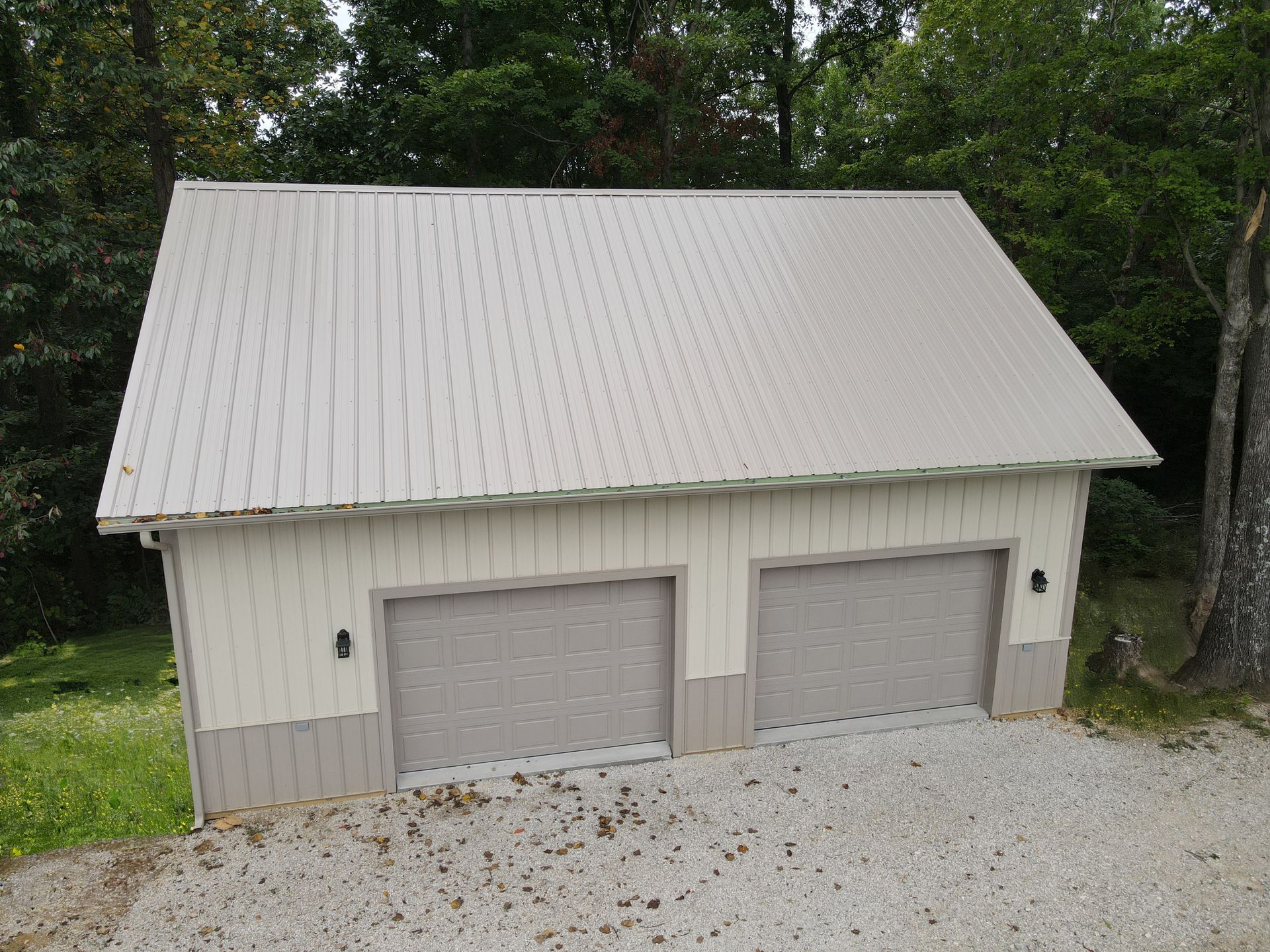 White detached two-car garage with a gray metal roof beside trees and grass.