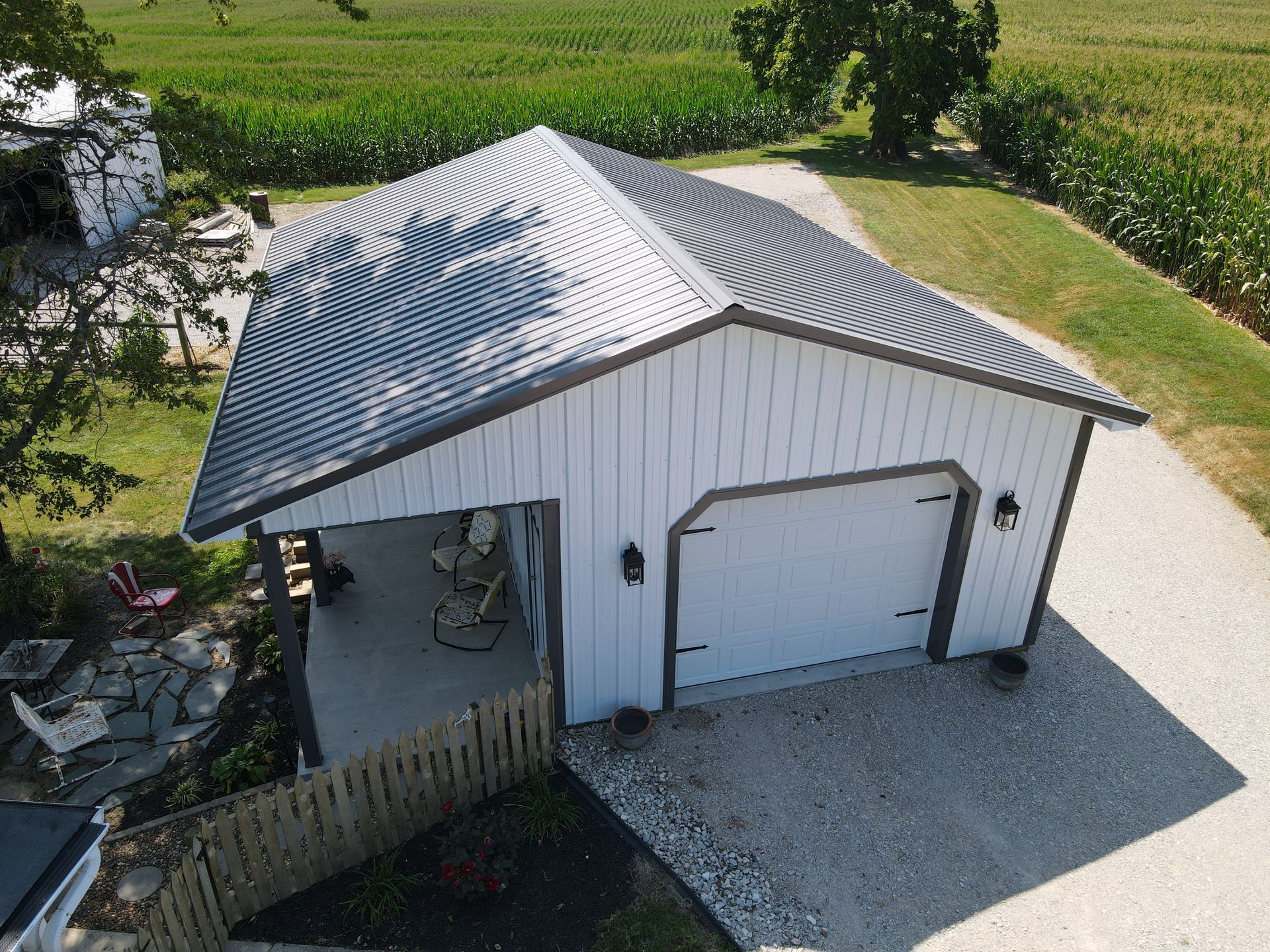 Aerial view of a white detached garage with a gray roof and gravel driveway beside a grassy field.