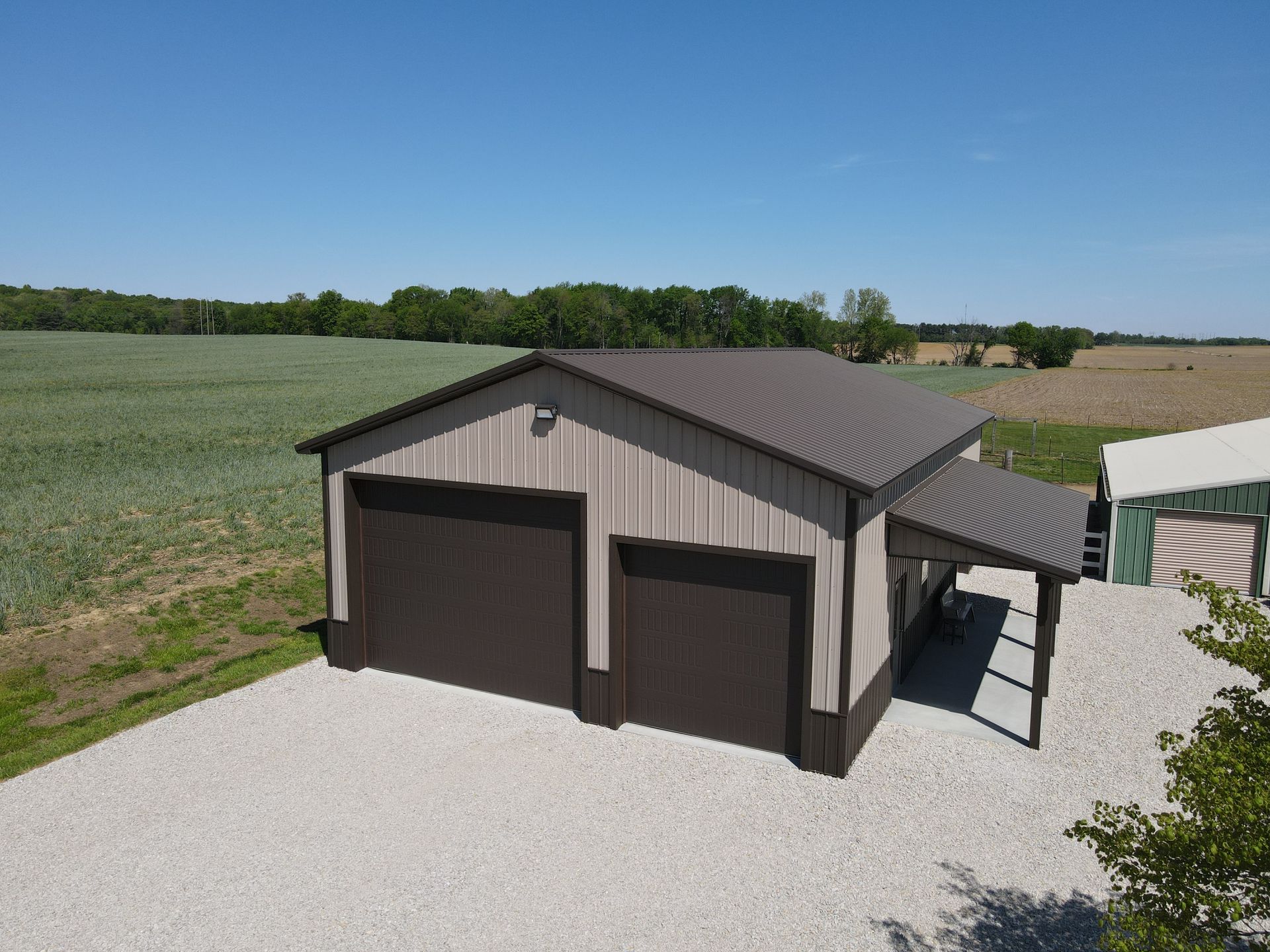Detached two-car garage with tan siding and dark roof on a gravel driveway in a rural field.