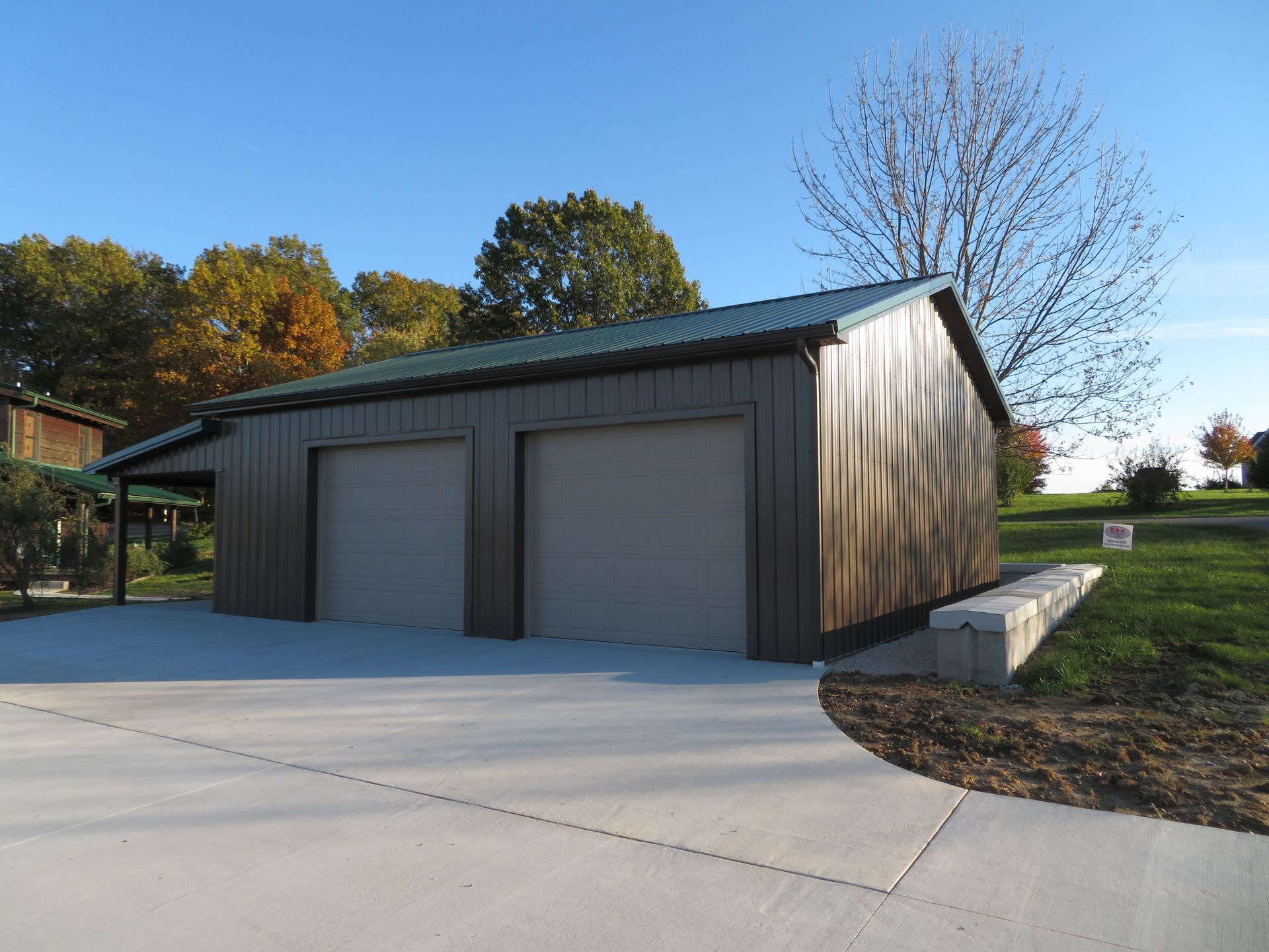Detached metal garage with two roll-up doors beside a concrete driveway on a sunny day