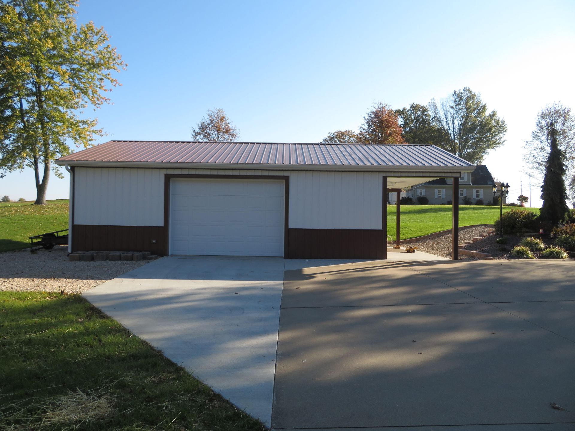 Single-car garage with white door and brown trim beside a driveway on a sunny day