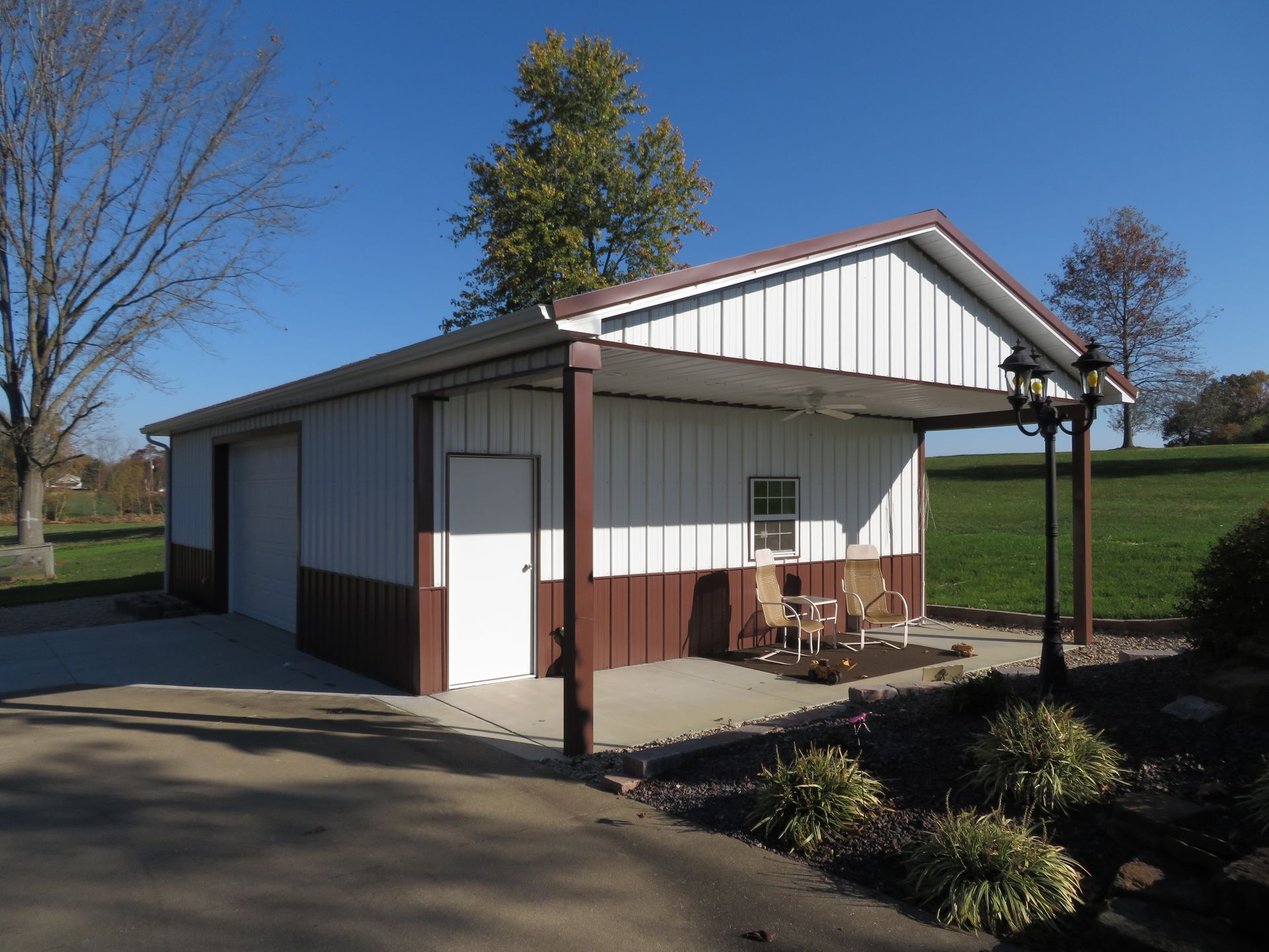 Small white utility building with red trim and a covered porch in a sunny rural setting