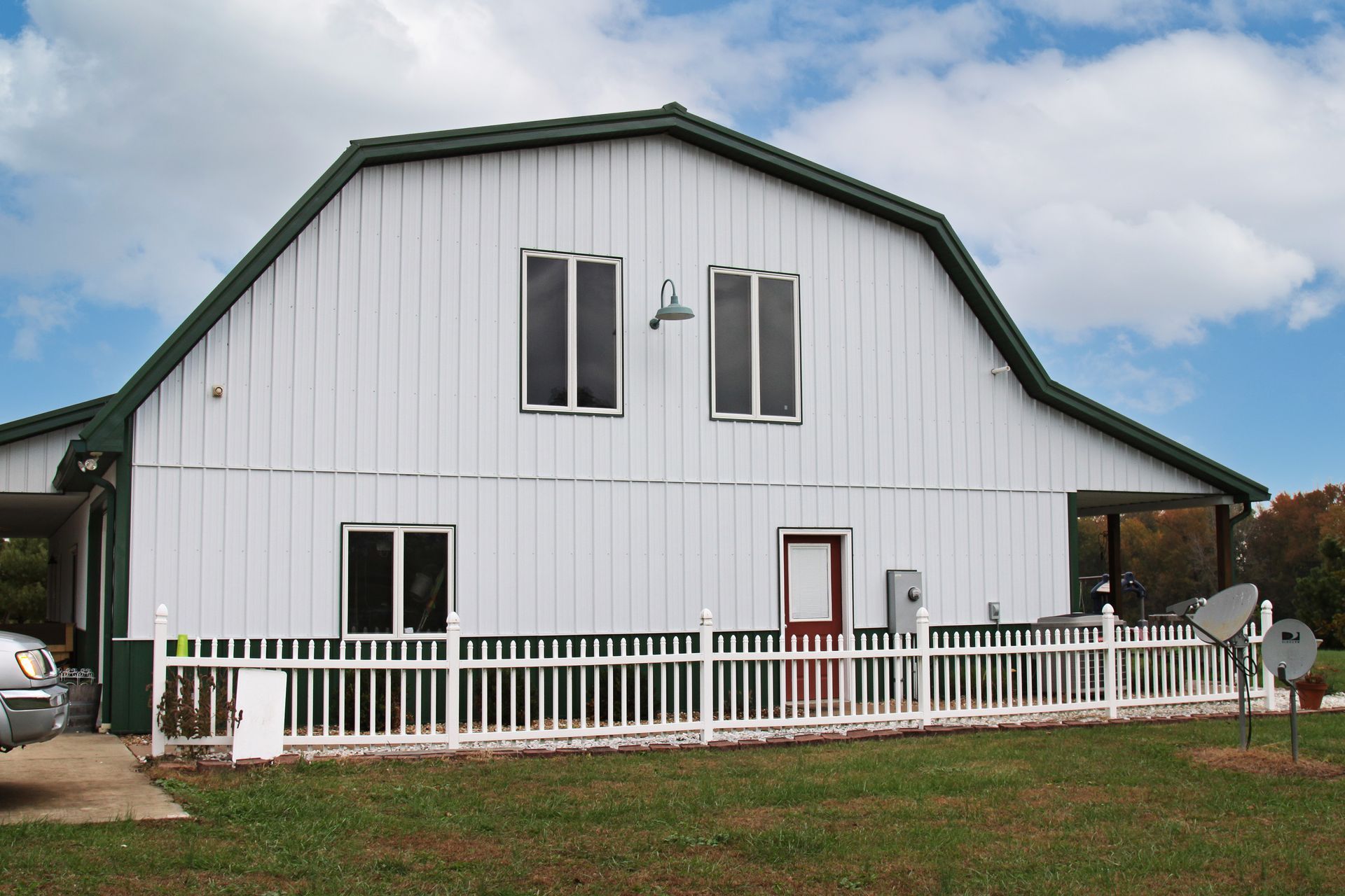 White barn-style house with green trim and a white fence under a cloudy sky