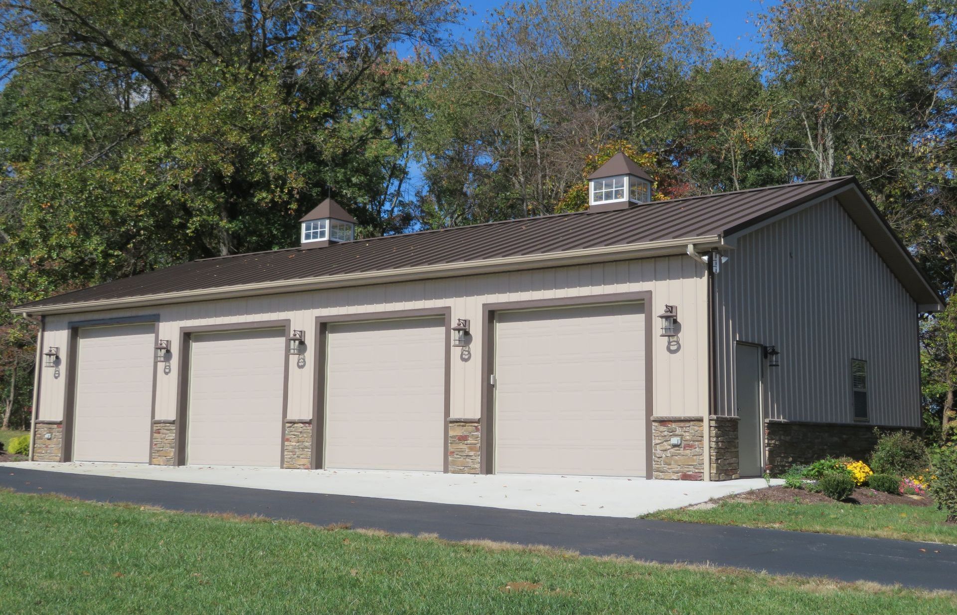 Two-car garage with four white doors, tan siding, and stone accents beside a paved driveway.