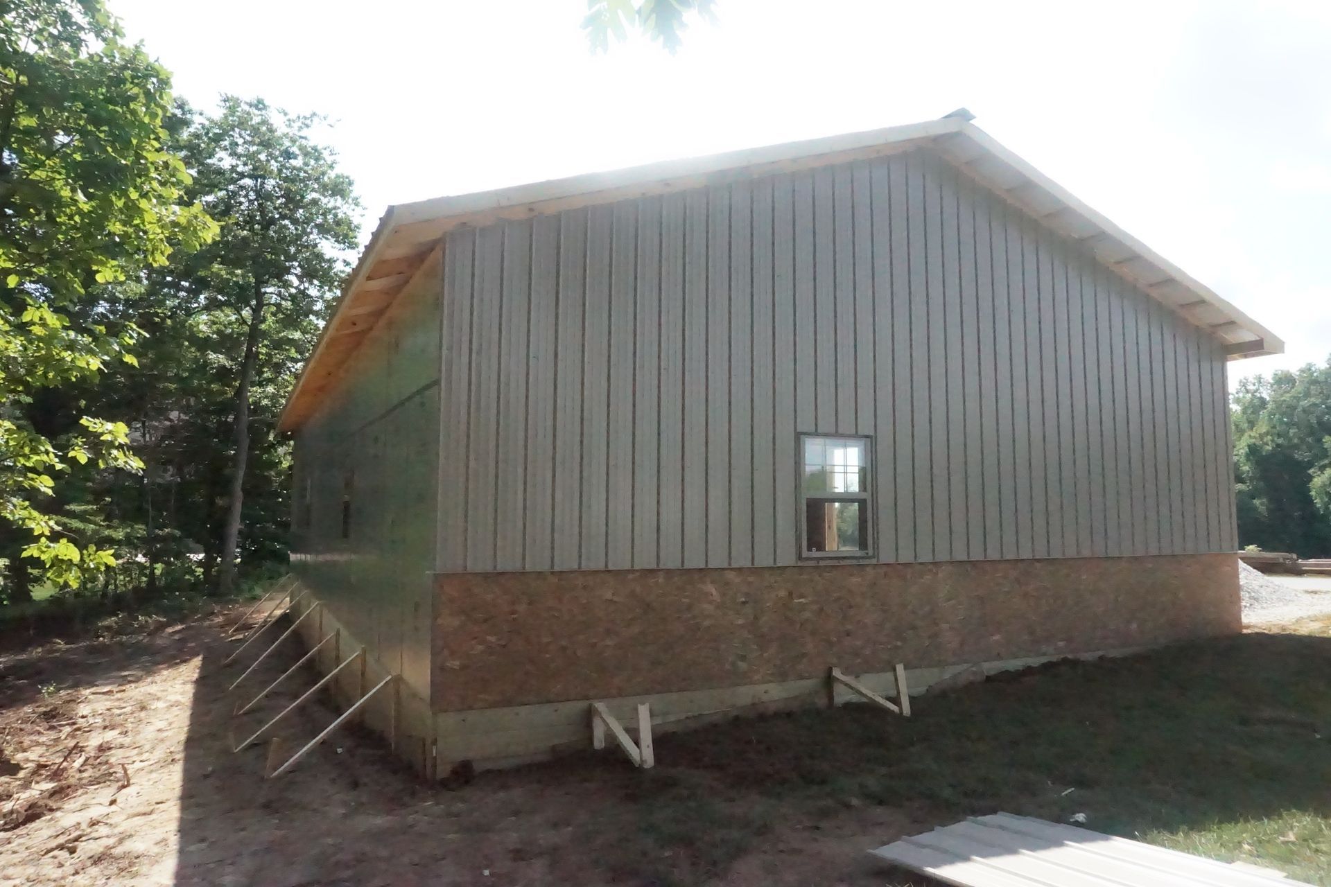 Small elevated wooden shed with a brick foundation, viewed from the side in a sunny wooded yard.