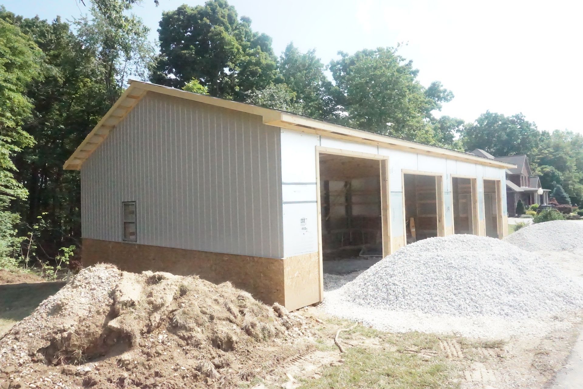 Small beige shed under construction with gravel piles and trees in the background