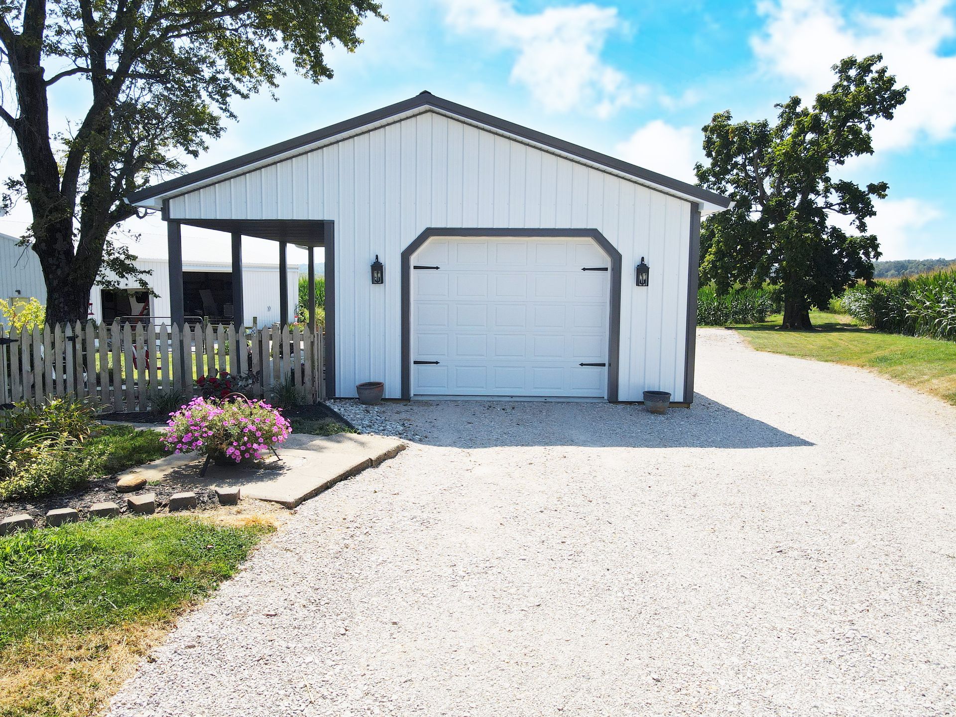 White detached garage with front door, gravel driveway, and flower bed on a sunny rural property