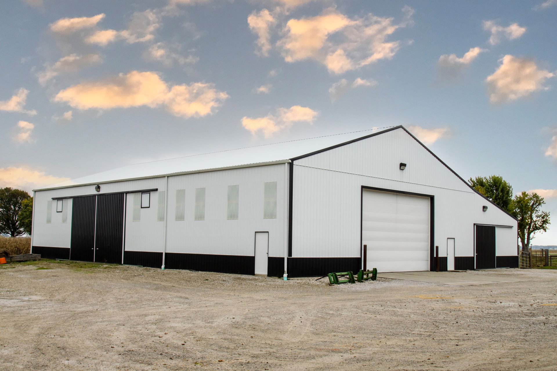 White metal warehouse building with large garage door on a gravel lot at sunset