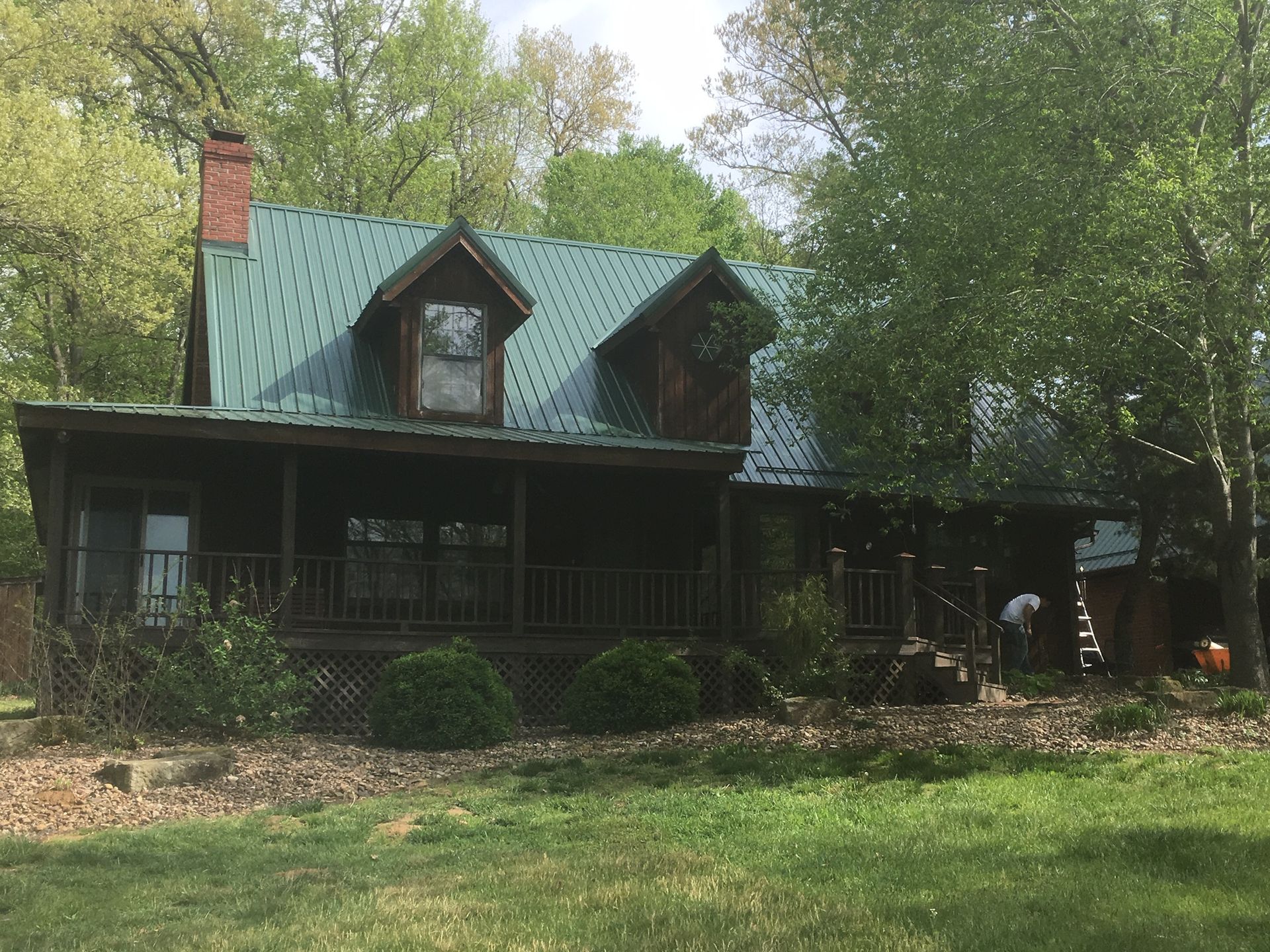Rustic green-roof cabin with dormer windows, surrounded by trees and a grassy yard