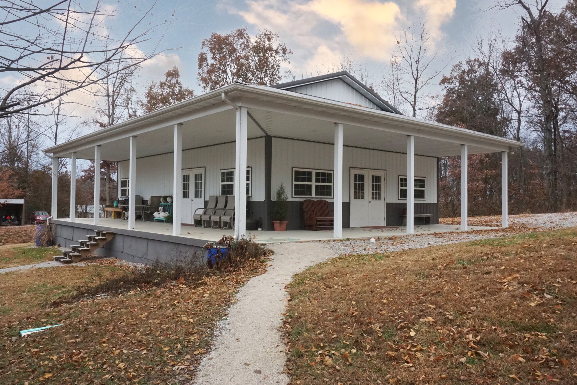 White wraparound porch on a house with a gravel path and autumn leaves under a cloudy sky.