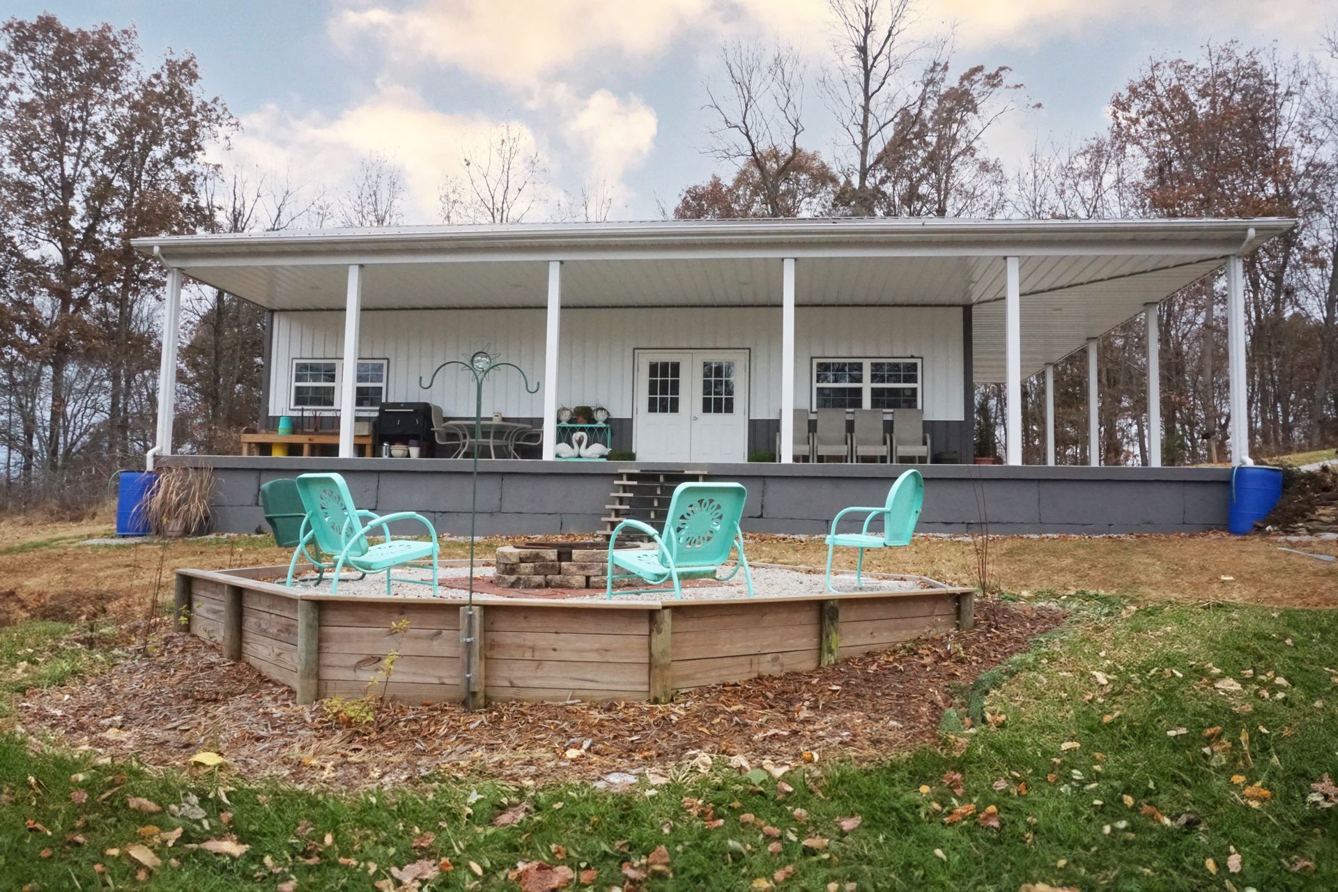 White house porch with columns, teal chairs, and a circular wooden deck in a fall yard