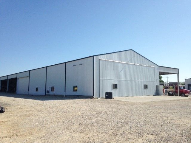 Large gray metal warehouse on a gravel lot under a clear blue sky