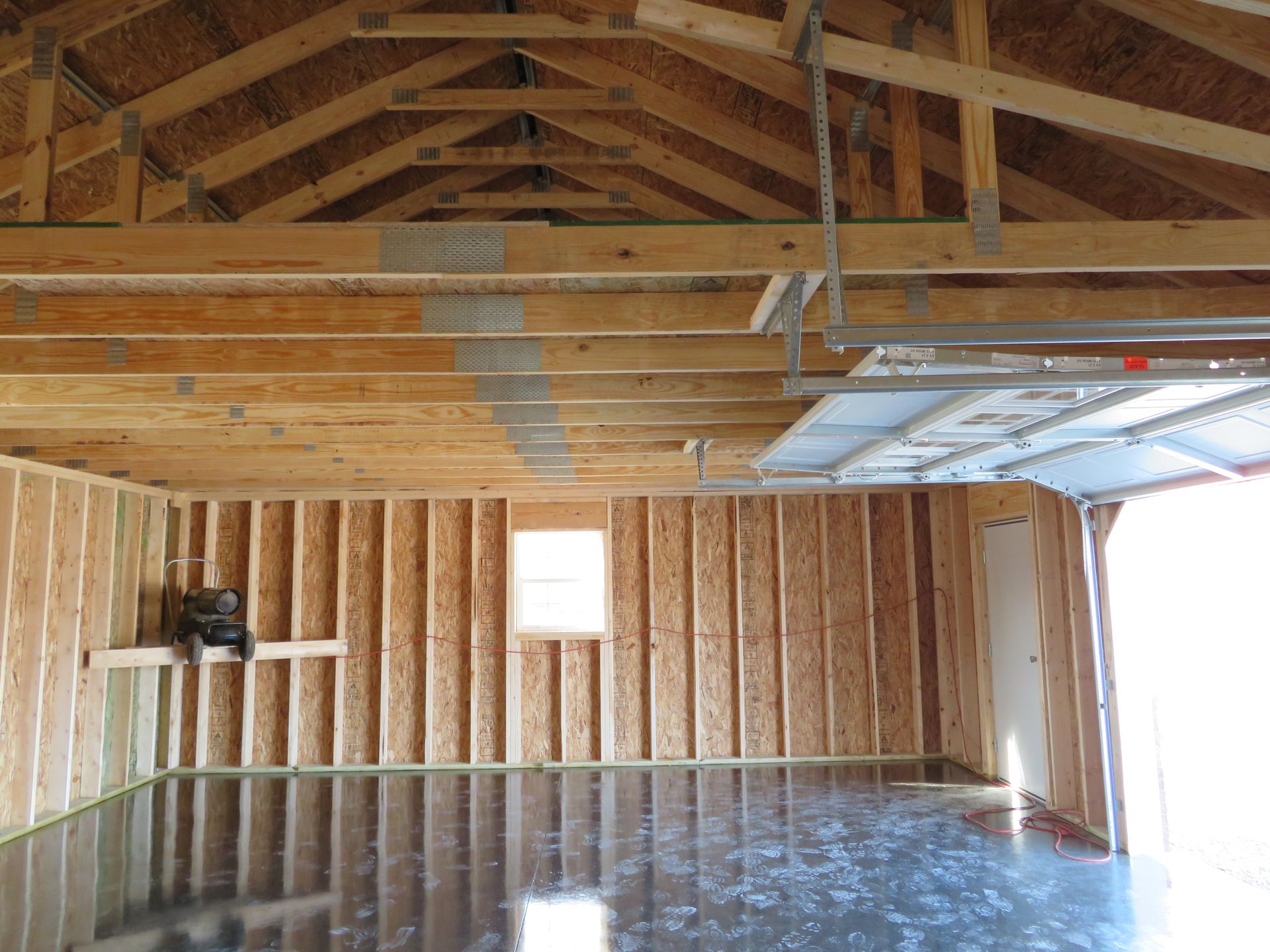 Empty unfinished garage interior with exposed wood framing and open garage door.