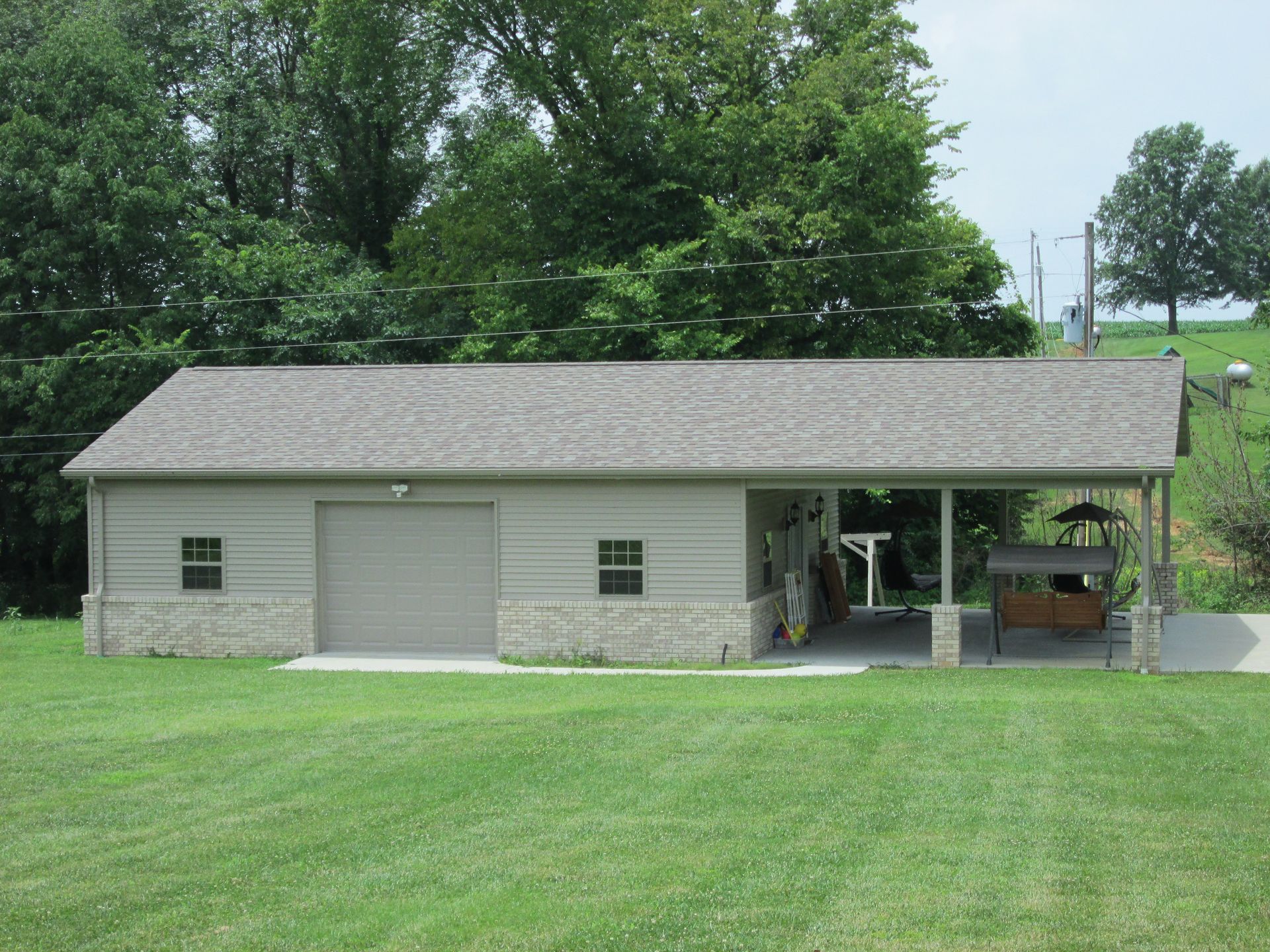 Gray garage/shed with open side, set in a grassy yard with trees in the background.