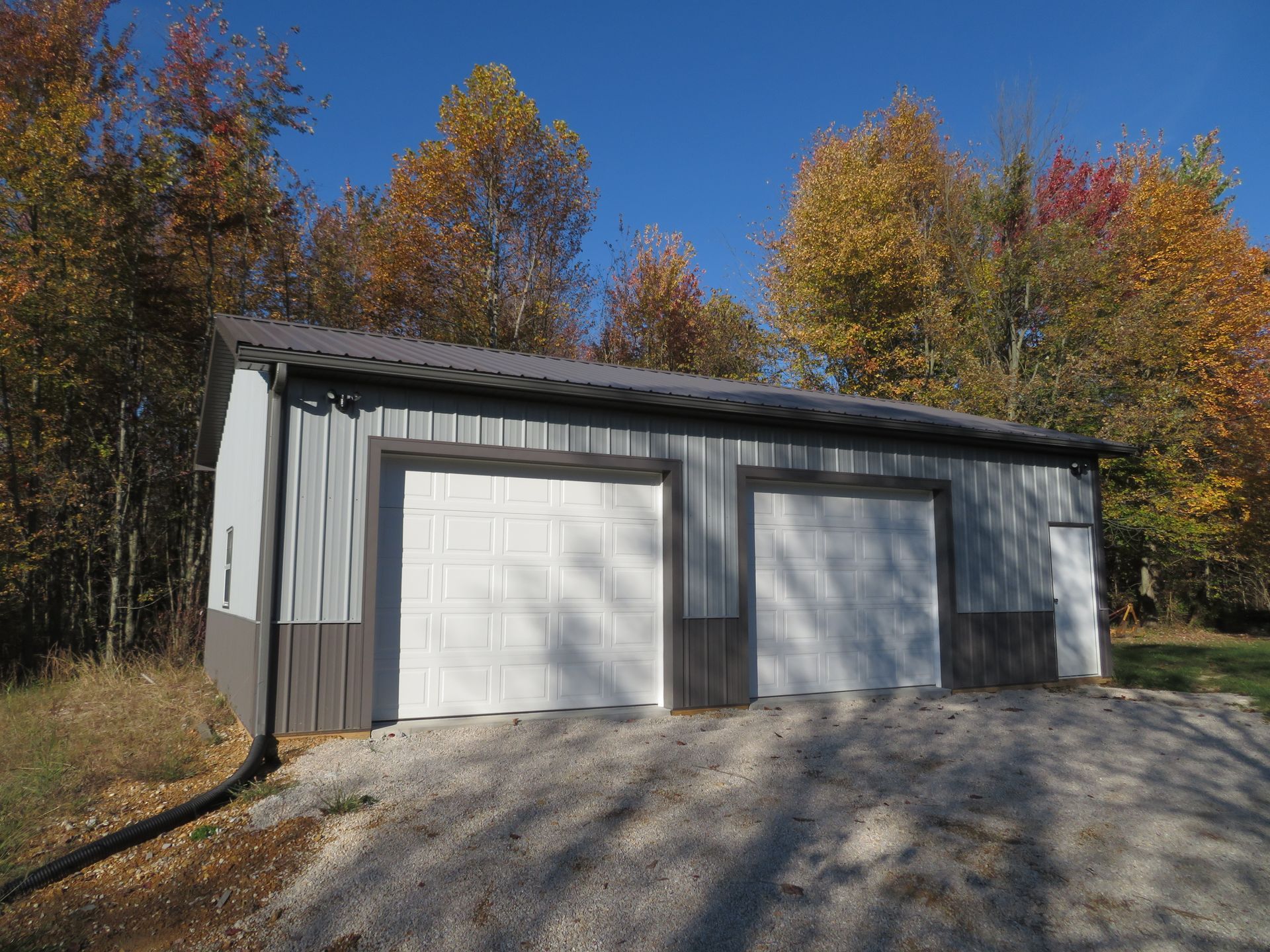 Detached white garage with three doors, gravel driveway, and autumn trees in the background