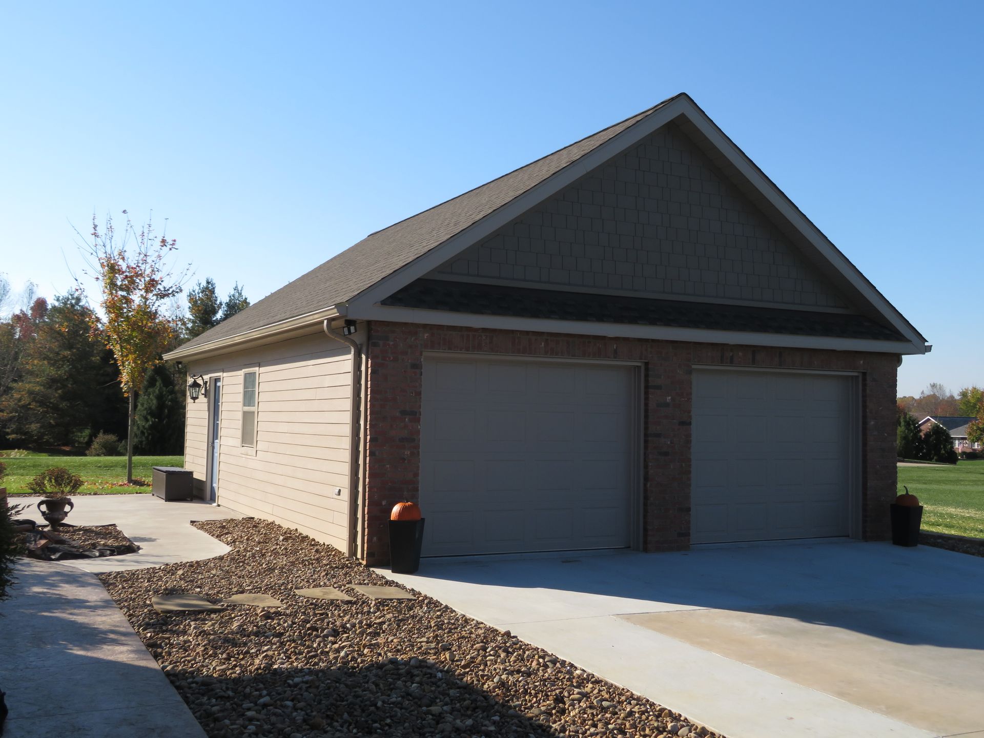 Detached beige garage with two gray doors and a dark gabled roof on a sunny day