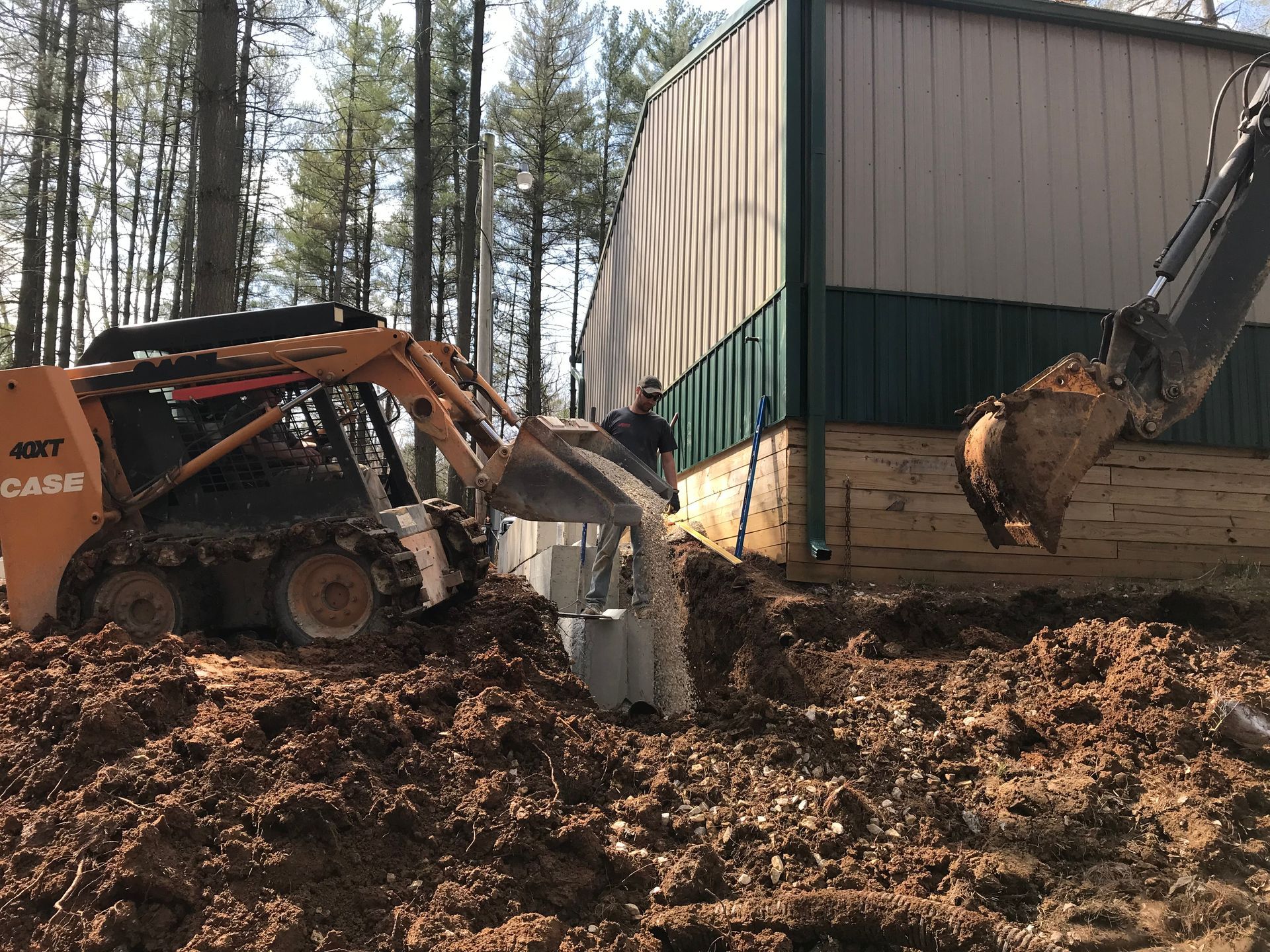 Construction equipment clearing mud beside a building in a wooded area