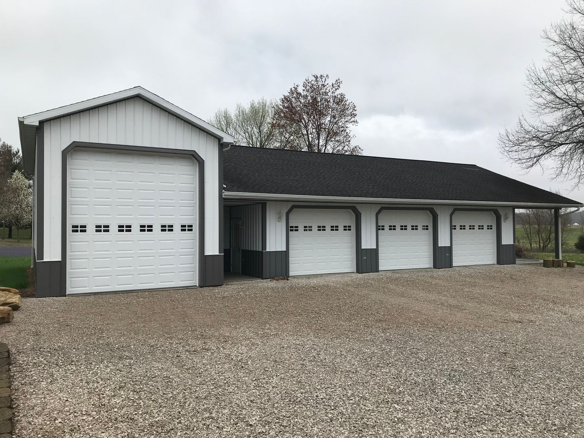 White garage with three small bays and one large bay on a gravel driveway under a cloudy sky