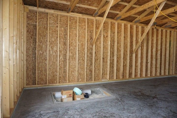 Unfinished wooden attic room with exposed framing and plywood floor, construction materials on the floor.