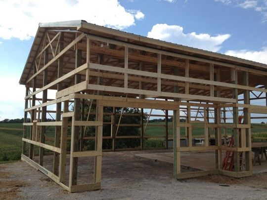 Wooden barn under construction with open framing and a large roof in a rural field.