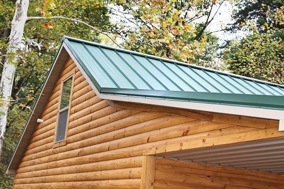 Wooden cabin roof with green metal panels and autumn trees in the background