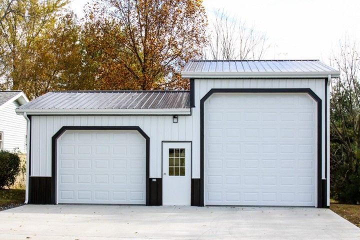 White detached garage with two roll-up doors and a small side entry, set against autumn trees.