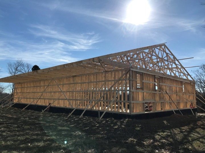 Partially built wooden house frame on a sunny hillside under a blue sky