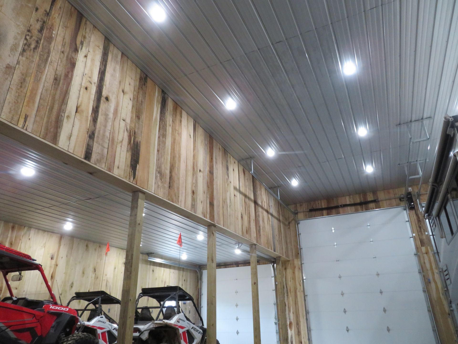 Indoor garage with red and black off-road vehicles under bright ceiling lights and white paneled walls