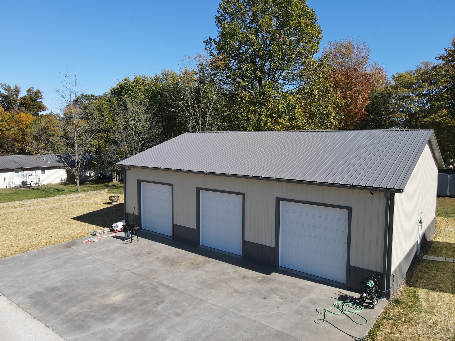 Detached garage with three white doors, gray siding, and a wide concrete driveway under a clear sky