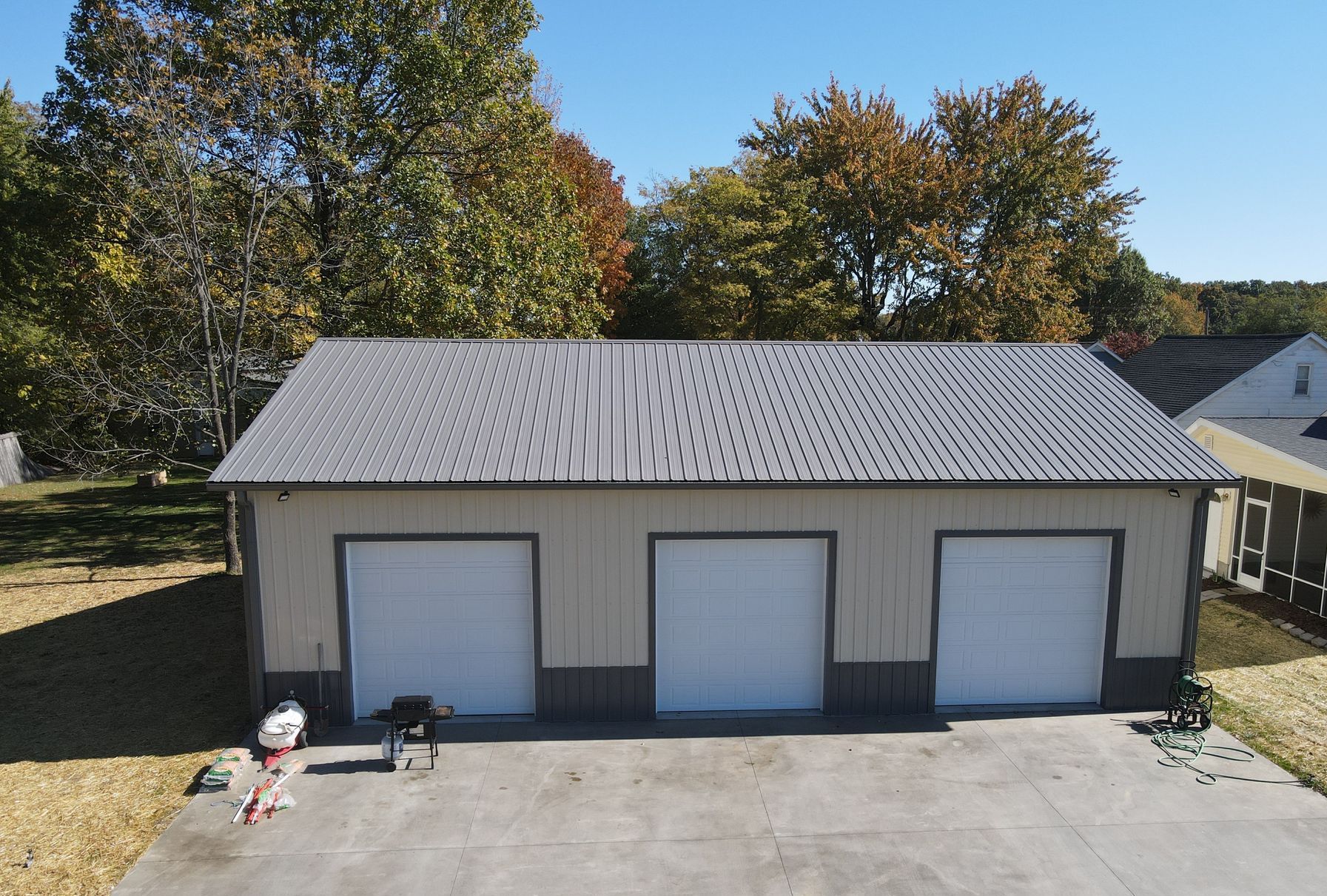 Three-bay detached garage with gray roof and white doors, viewed from a driveway, trees in the background
