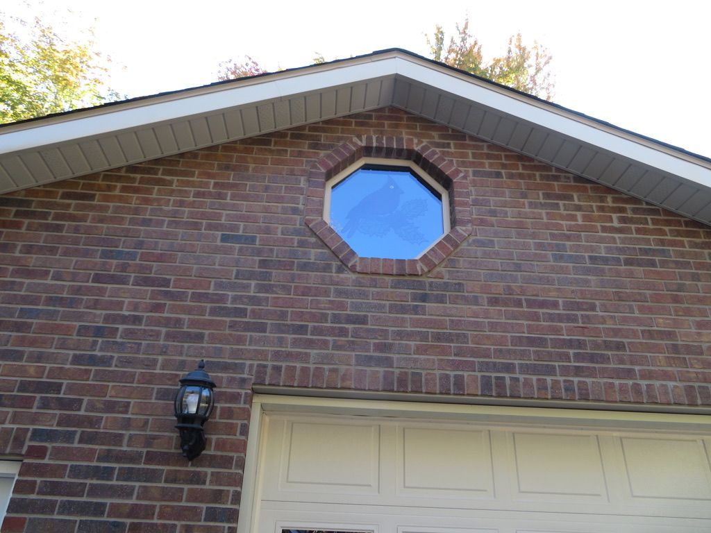 Brick house front with a small octagonal attic window and garage door below