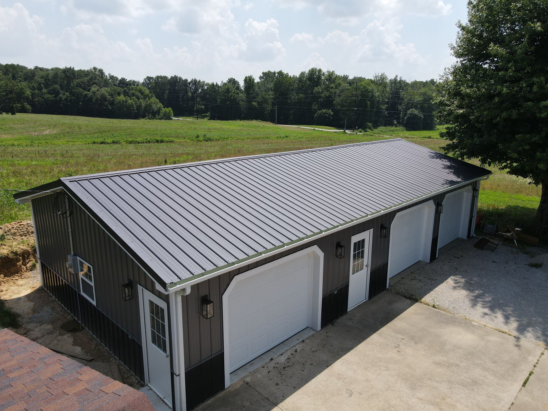 Gray metal garage building with white doors beside a concrete driveway and grassy field