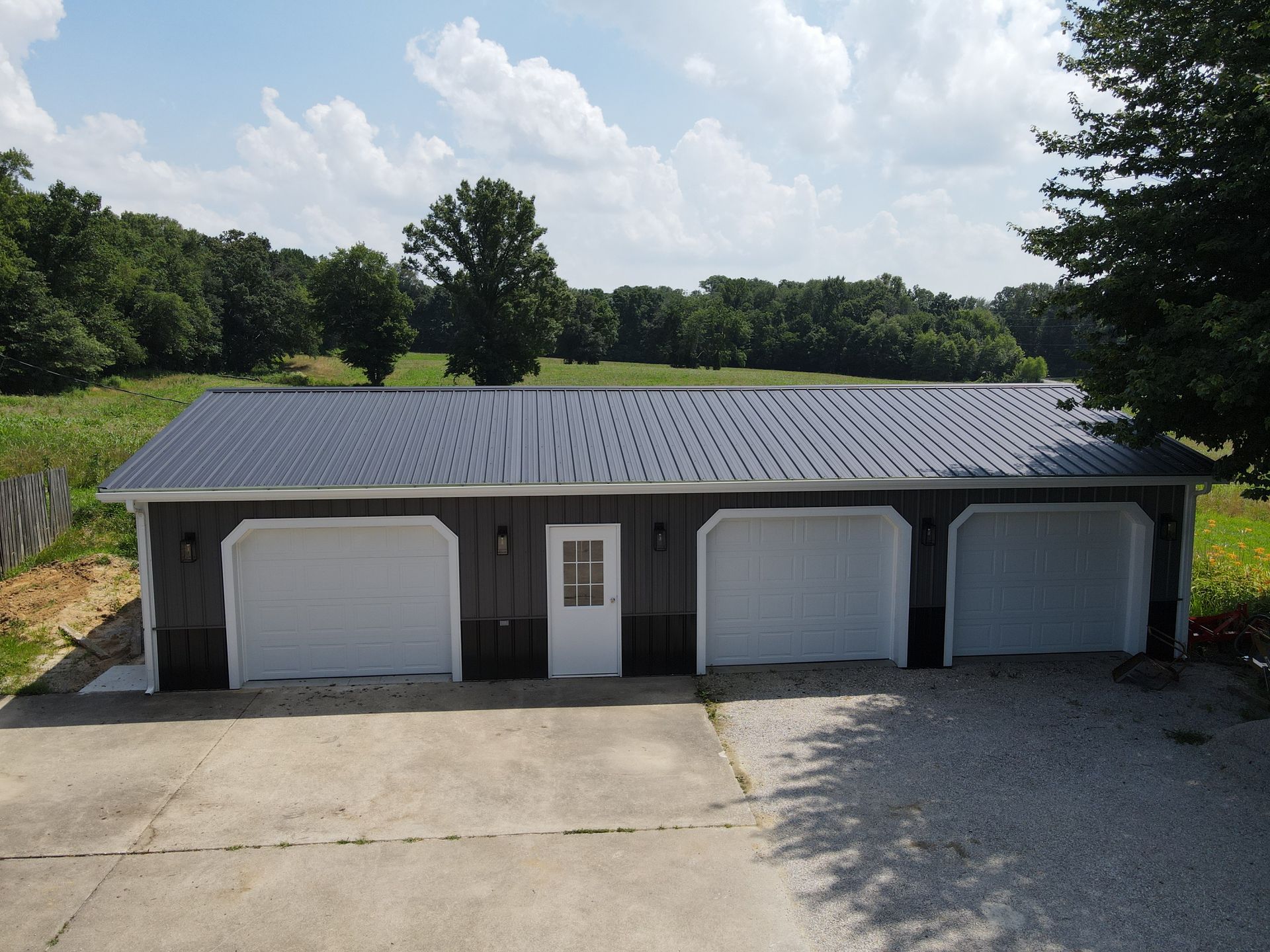 Three-car garage with a dark roof and white doors, viewed from a paved driveway in a rural setting.