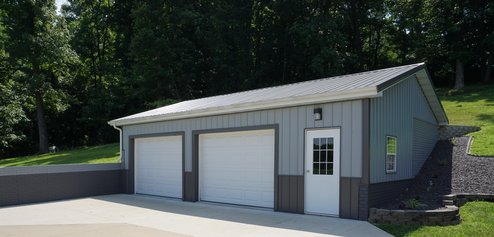 Gray two-car garage with white doors and a side entry door on a sloped driveway.