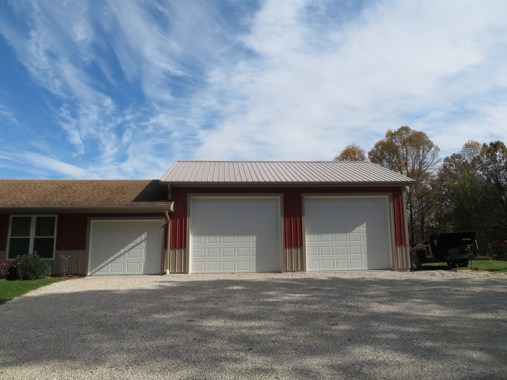 Three garage bays in a gravel driveway beneath a partly cloudy sky.