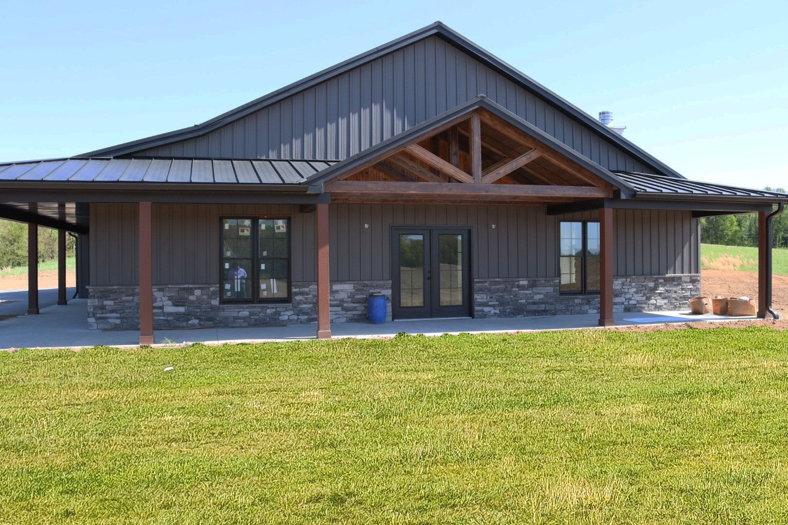Modern single-story house with dark metal roof, wood columns, and a large green lawn.