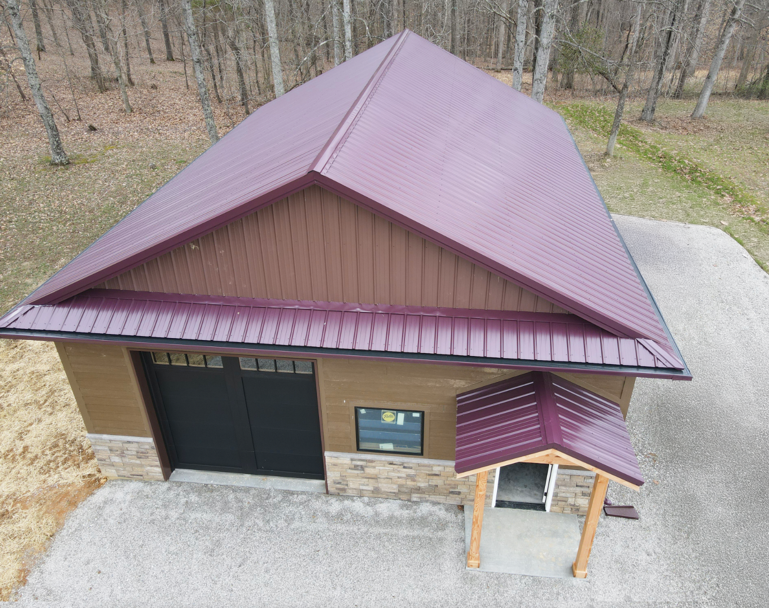 Aerial view of a small building with a maroon roof, stone walls, and a covered entrance on gravel.