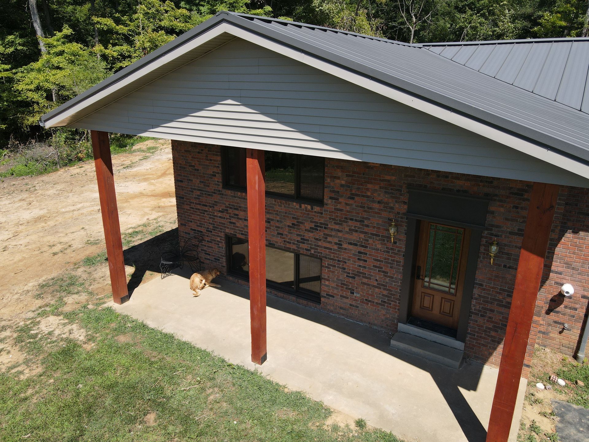 Brick house porch with red posts, concrete floor, and dark metal roof