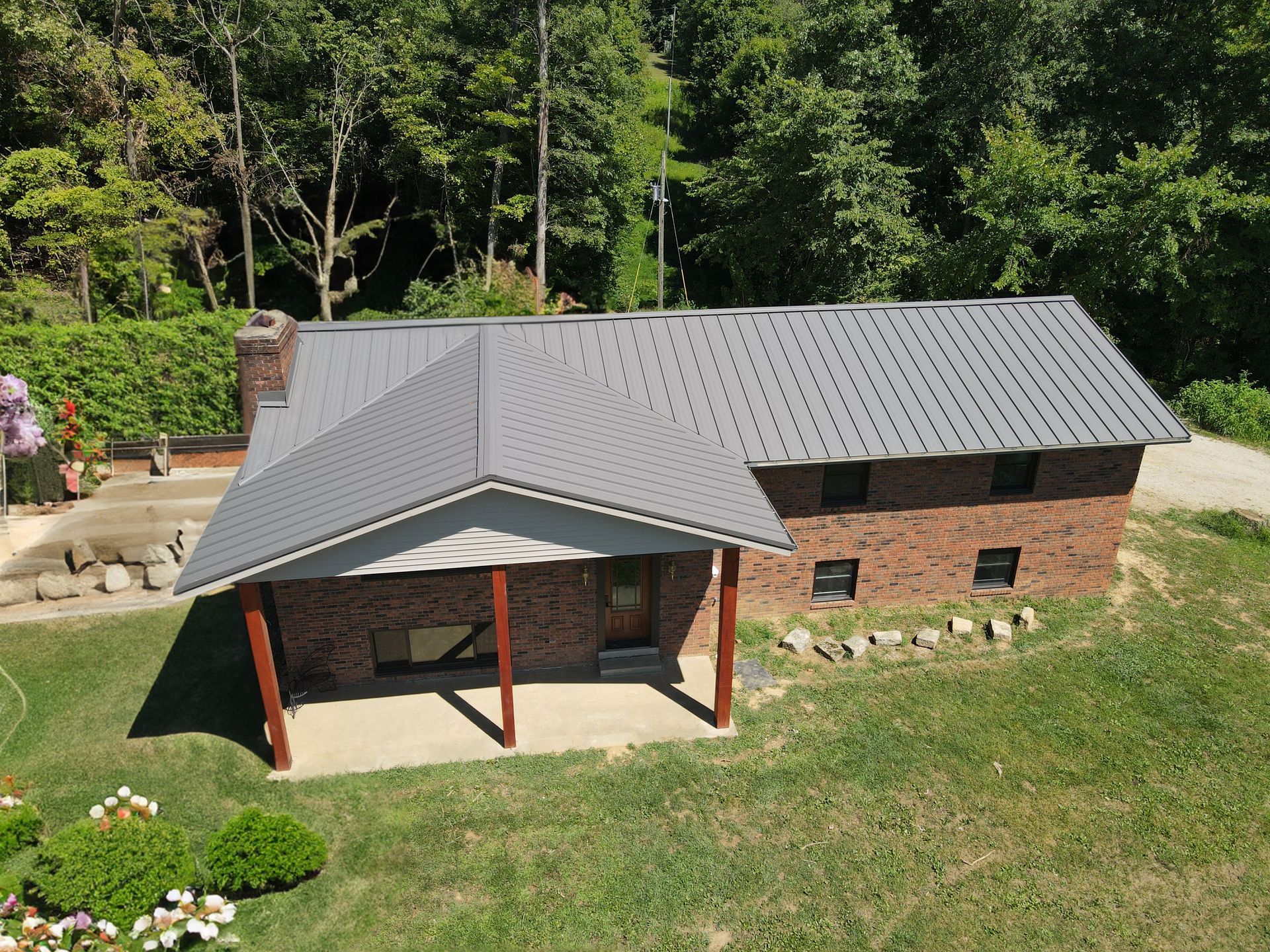 Aerial view of a small brick building with a gray metal roof and covered porch, surrounded by grass and trees.