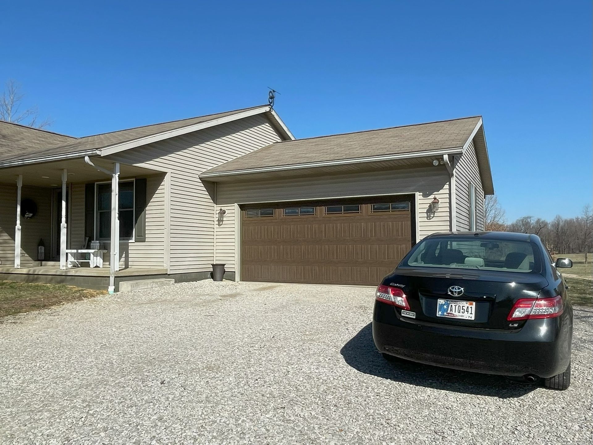 Black sedan parked in a gravel driveway in front of a tan house with a two-car garage.