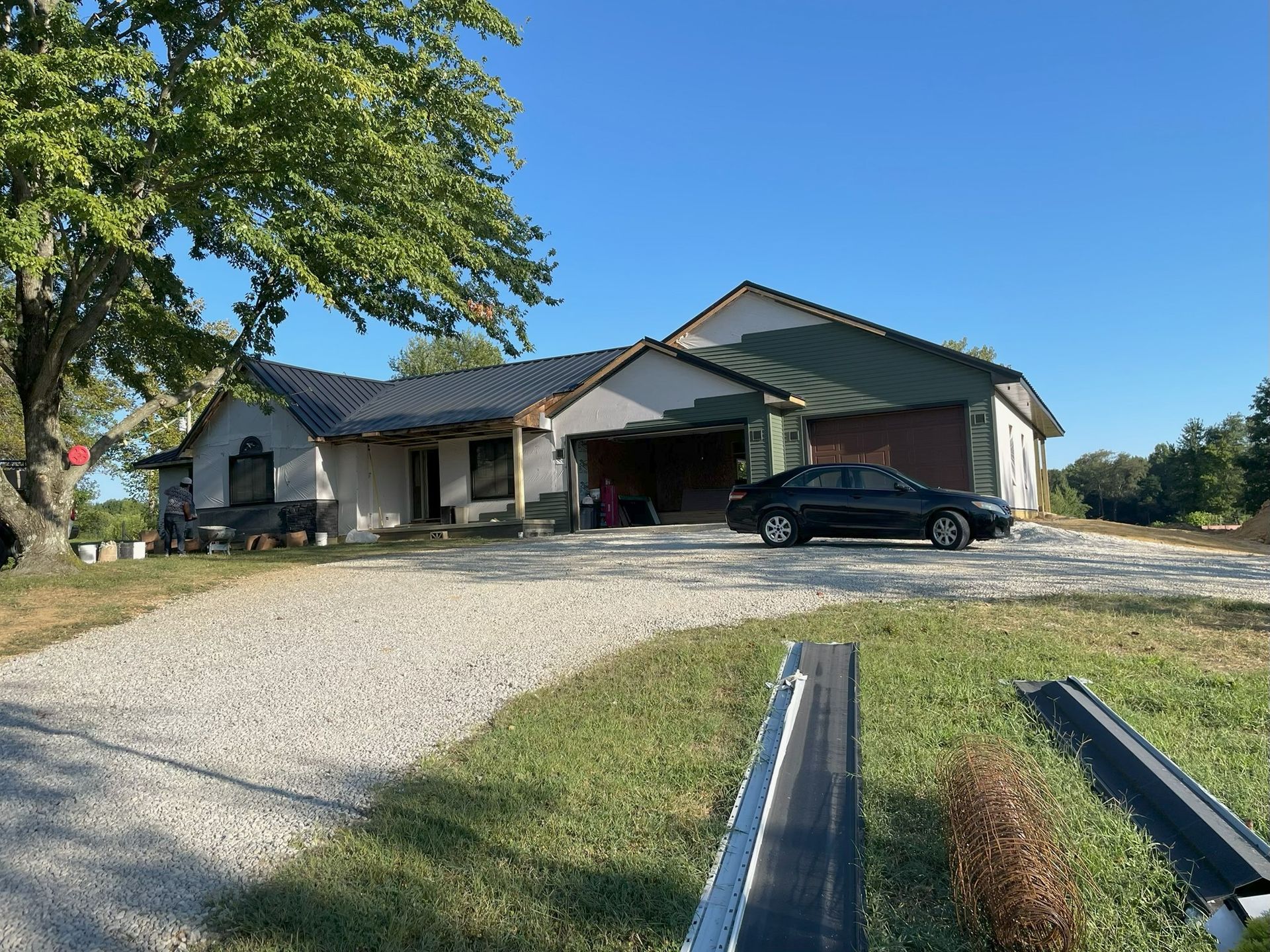 Suburban house with gravel driveway, carport, and parked black car on a sunny day