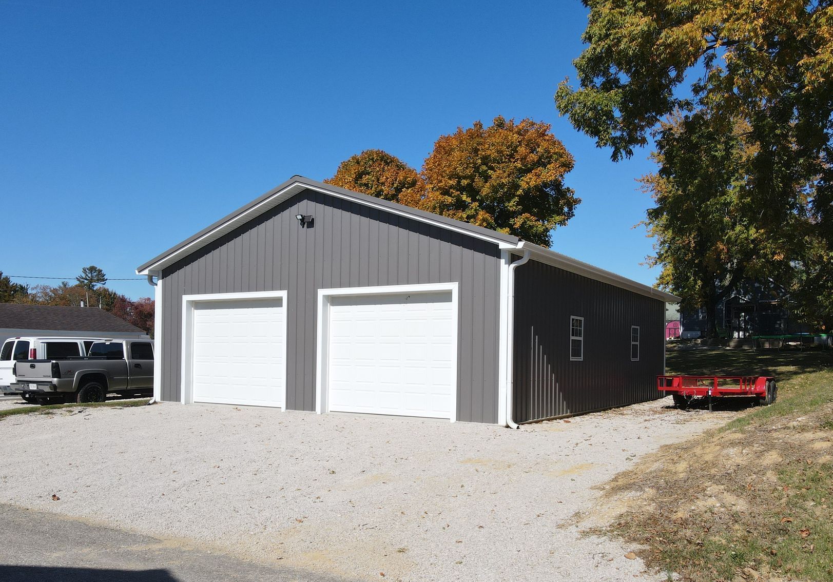 Gray metal garage with two white doors on a gravel driveway under a clear blue sky