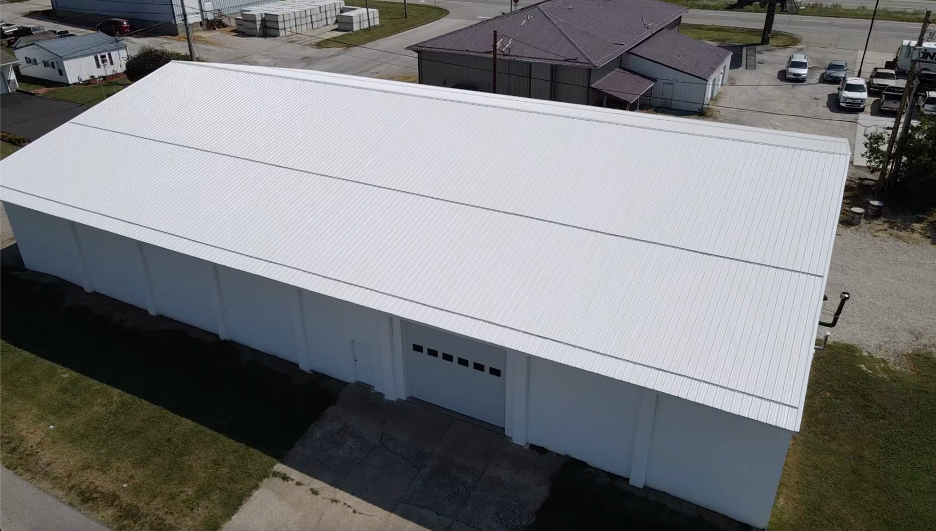 A large white metal warehouse with a peaked roof and garage doors, viewed from above.