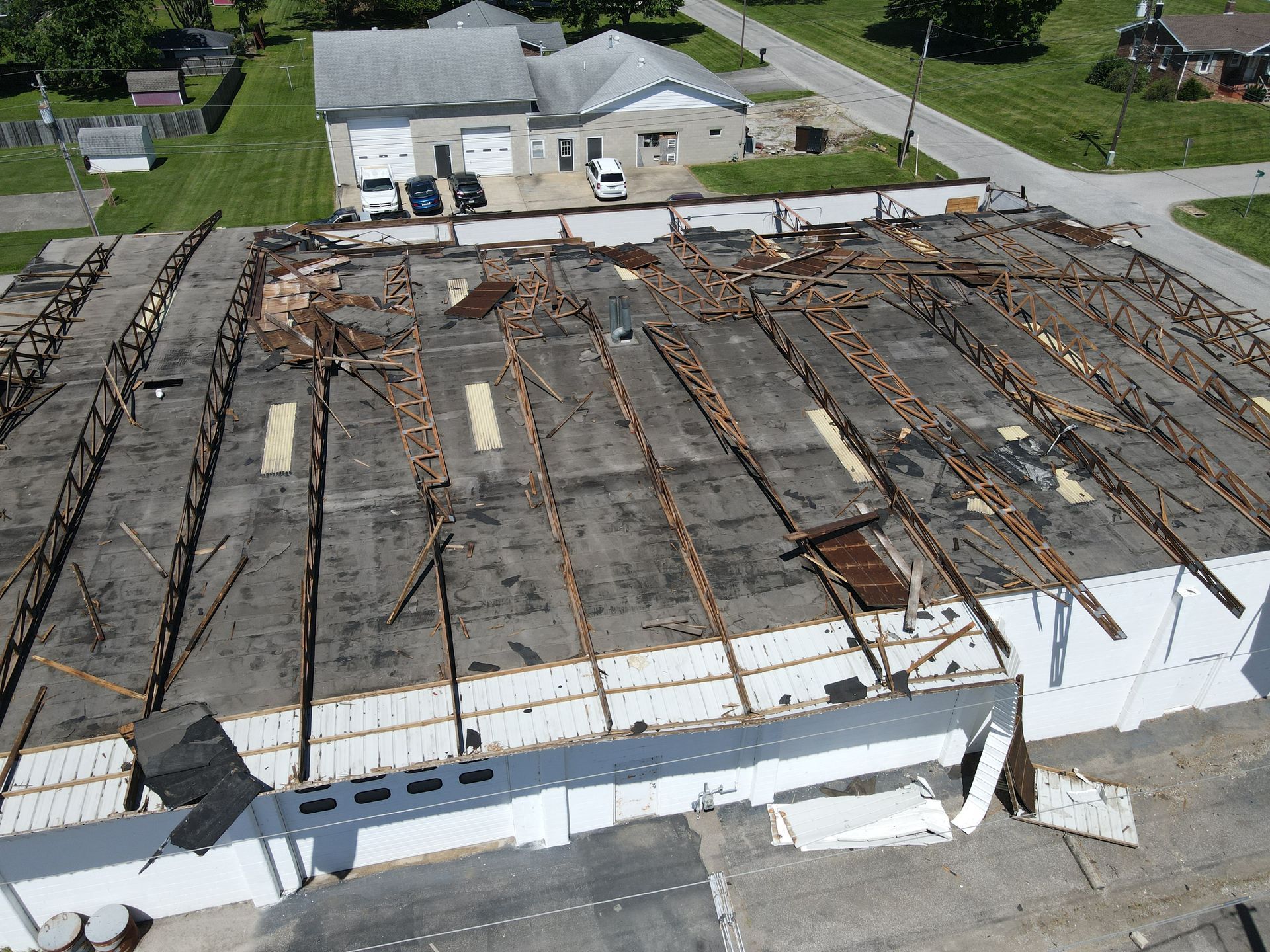 Aerial view of a collapsed roof on a white building with exposed rusted beams and debris nearby.