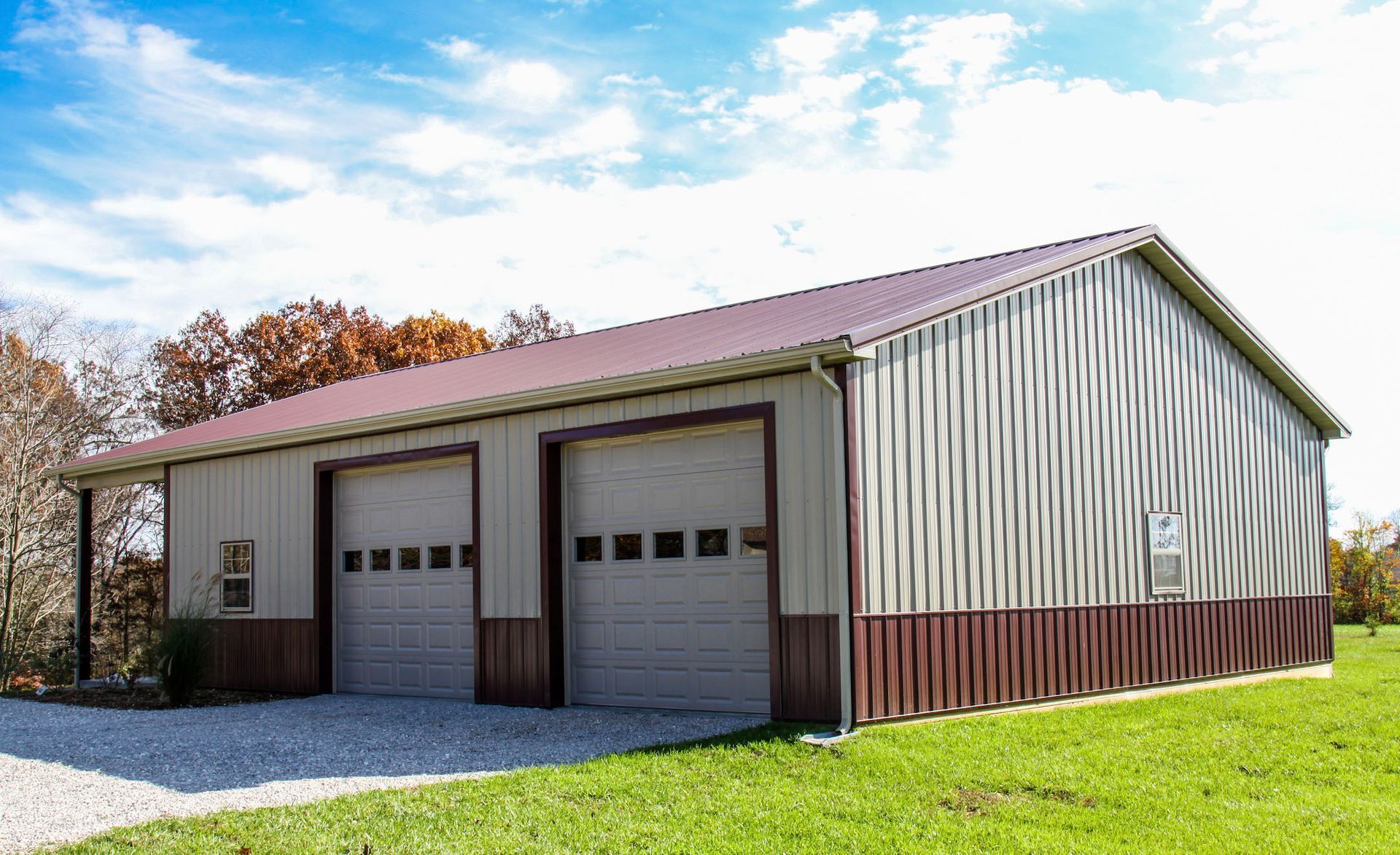 Detached two-bay metal garage with white siding, red roof, and gravel driveway under a blue sky