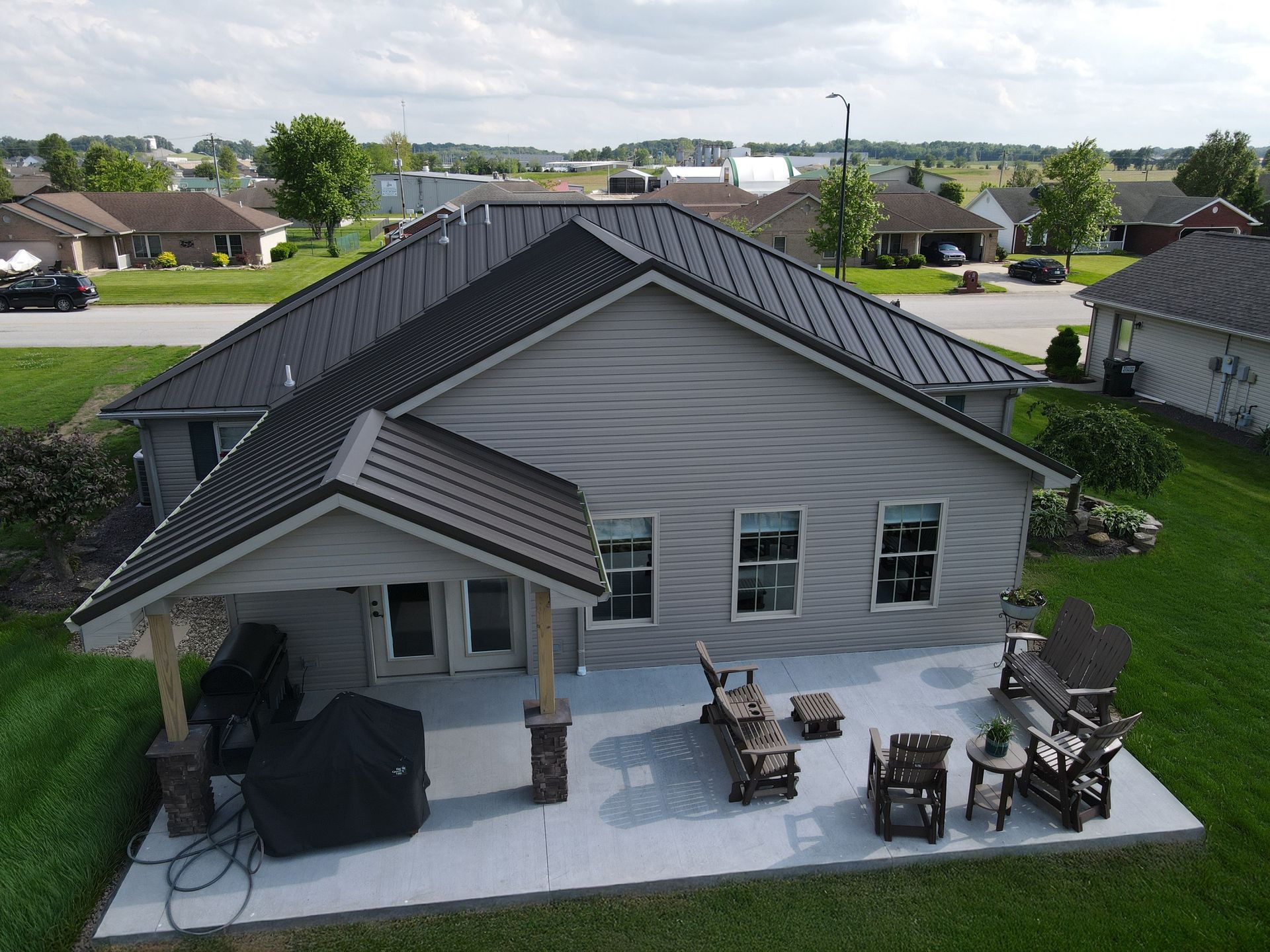 Aerial view of a gray suburban house with a covered patio, backyard furniture, and neighboring homes nearby