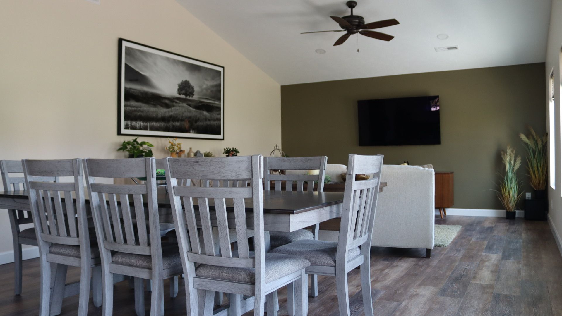 Dining area with white chairs, dark table, wall art, ceiling fan, and wall-mounted TV in a modern room