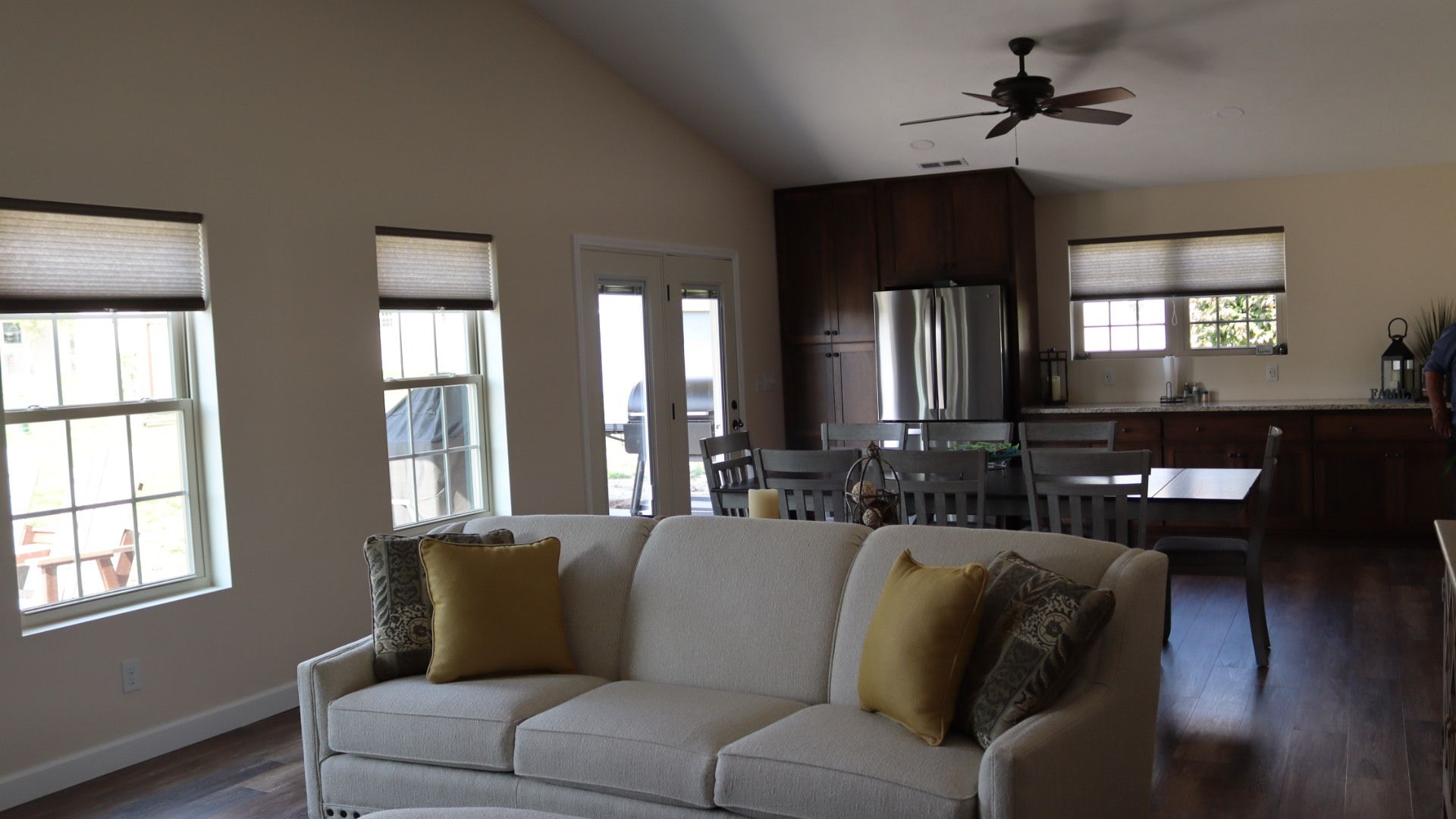 Bright living room with a white sofa, windows, ceiling fan, and dining area in the background