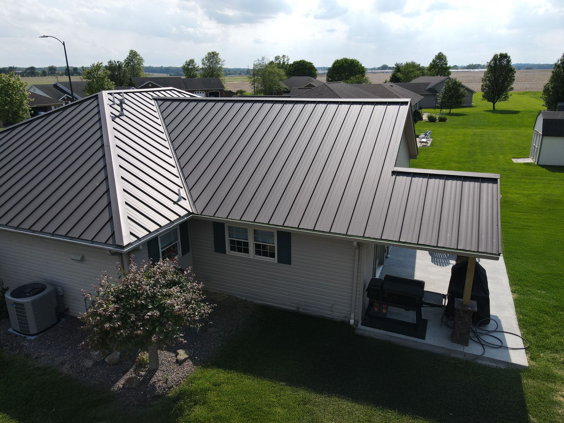 Single-story house with gray metal roof, white siding, and a covered patio in a suburban yard.